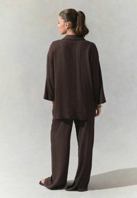 Brune, afslappede bukser og en matchende langærmet skjorte med en struktureret stof og krave. Minimalistisk design med brede ærmer.