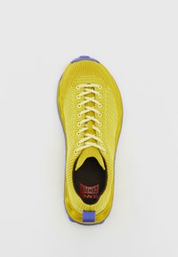 Κίτρινο πλεκτό αθλητικό παπούτσι με μοβ λεπτομέρειες στη σόλα, στρογγυλή μύτη και λευκά κορδόνια. Το εσωτερικό διαθέτει σκούρα εσωτερική σόλα με branding.