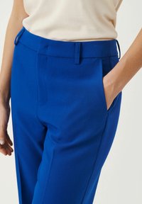 Pantaloni blu su misura con vestibilità slim, tasche laterali, tessuto morbido e design frontale piatto. Include passanti per cintura per una vestibilità regolabile.