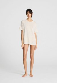 Kort beige oversized t-shirt lavet af tekstureret stof, med rund halsudskæring og korte ærmer, båret med minimal benbeklædning.