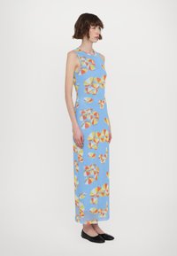 Robe longue, bleu clair, ornée d'un motif géométrique en jaune, orange et rouge. Fabriquée à partir d'un tissu lisse avec une silhouette ajustée.