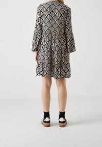 Vestido a rayas en blanco y negro con un diseño en capas y mangas de campana, combinado con calcetas negras y zapatillas en blanco y negro.