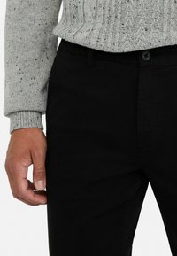 Pantalones negros con una textura suave y un ajuste entallado, combinados con un suéter de punto gris claro que presenta un patrón de canalé.