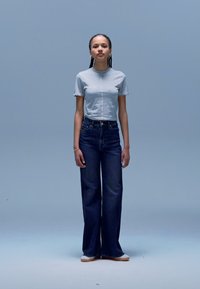 T-shirt cinzenta de manga curta combinada com jeans escuros de ganga clara, com cintura alta e pernas largas, completada com ténis suaves e de cor clara. Estilo simples e casual.