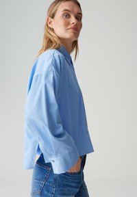 Camicia azzurro chiaro a maniche lunghe con bottoni, vestibilità comoda e spacchi laterali. Tessuto liscio, colletto classico e polsini sagomati.