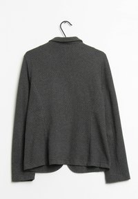 Blazer noir en tissu texturé, présentant un motif discret à pois blancs, un col à revers et un dos ouvert. Suspendu à un crochet.