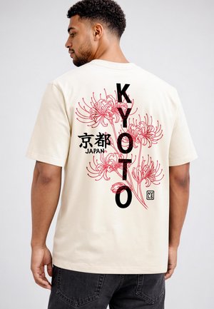Man wearing off-white t-shirt with red floral design and black text reading "KYOTO" and "Japan" in Japanese and English on the back.