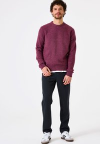 Bordeaux gebreide sweater met ronde hals, geribbelde manchetten en onderrand, gecombineerd met donkere broeken en witte sneakers met zwarte strepen.