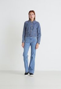Veste en jean clair avec un col, fermeture à boutons, deux poches avant, associée à un jean flare bleu clair et des chaussures noires décontractées.
