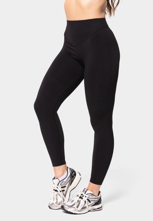 Black high-waisted leggings with a smooth texture and fitted design, paired with silver and black athletic shoes featuring white laces.