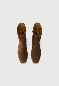 Bottines en suede marron avec un bout pointu et une texture lisse, dotées d'une fermeture éclair sur le côté et d'une semelle plus claire qui contraste.