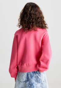Felpa rosa con polsini e orlo a costine, caratterizzata da una vestibilità rilassata. Indossata con pantaloni corti in denim blu chiaro con effetto lavato acido.