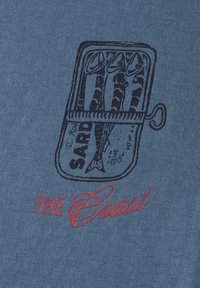 Modrá džínová tkanina s grafikou sardinek v plechovce, obkrouženou tmavě modrou, s nápisem "THE Coast" červeným kurzívou pod ní.