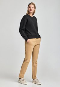 Svart sweatshirt med rund hals och muddar, i kombination med beige byxor och ljusa sneakers. Enkelt och rent design.