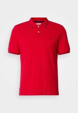 Polo shirt rossa in cotone, con collare classico, chiusura a due bottoni e dettagli a righe blu sulle maniche e sul colletto. Logo GANT presente.