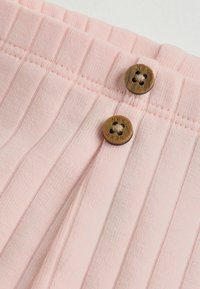 Nahaufnahme eines hellrosa strukturierten Stoffs mit zwei braunen Knöpfen, auf denen jeweils das Wort "NEXT" eingraviert ist.