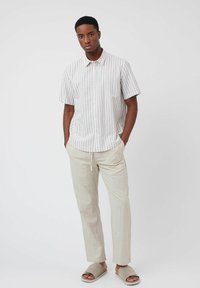 Chemise à manches courtes rayée dans des couleurs claires, associée à un pantalon en lin beige et des sandales gris. Présente un design à boutons.