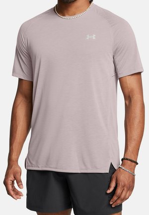 Mężczyzna ubrany w jasnofioletową sportową koszulkę Under Armour z krótkim rękawem i czarne spodenki, ozdobiony bransoletkami i naszyjnikiem z koralików.