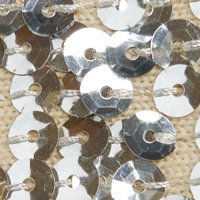 Des embellissements en sequins argentés disposés très près les uns des autres, de forme ronde avec des trous centraux, surface brillante, réfléchissant la lumière sur un fond beige.