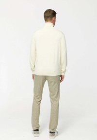 Fehér pulóver magas gallérral, világos mintás nadrággal párosítva. Sima felület és laza fazon, oldalsó zsebekkel a nadrágon.