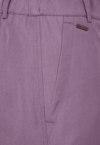 Lila tygbyxor med en strukturerad finish, sidofickor och en metallisk märkesetikett. Rena linjer och skräddarsydd design med synlig sömnad.
