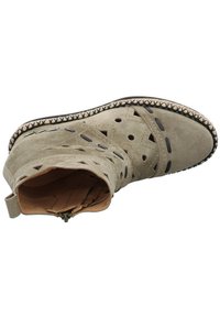 Botín de ante en beige claro con diseños troquelados, detalles cosidos y un interior marrón texturizado. Presenta una punta redondeada y un tacón bajo.