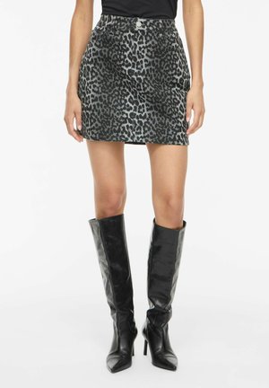 Kvinde iført en sort og grå leopard-print miniskørt kombineret med sorte knæhøje spidse støvler med hæl.
