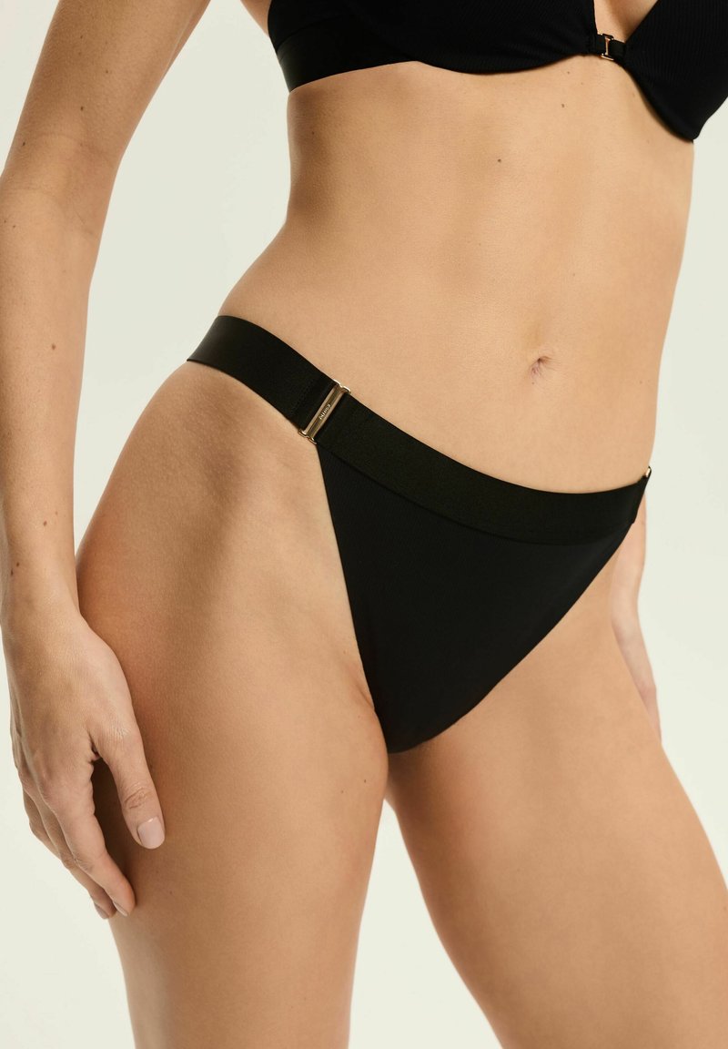 Czarne majtki bikini wykonane z teksturowanej tkaniny, z wąskim paskiem w talii ozdobionym złotym metalowym zapięciem.