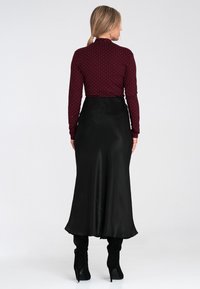 Długa czarna satynowa spódnica w połączeniu z bordową bluzką z długim rękawem, pokrytą białymi kropkami. Bluzka ma wysoki dekolt oraz dopasowany krój.