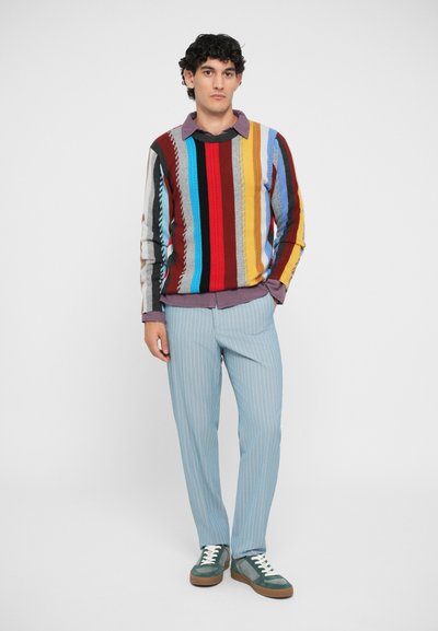 Multicolored striped sweater with varying widths of red, blue, and yellow; light blue pinstriped trousers; green sneakers with white laces.