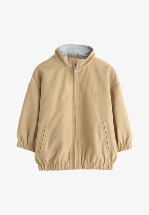 Beige jakke med lynlås, elastiske manchetter og kant, to forlommer, høj krave med ternet inderfor og et lille sol-emblem på brystet.