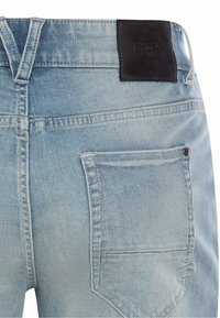 Light blue denim jeans back view showing a single pocket and a black Camel Active brand label on the waistband.