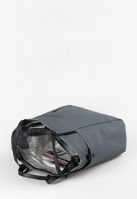 Grå vandtæt rygsæk med sorte håndtag, der har et rummeligt indre med et gittermønster og røde detaljer. Lynlåslommen er synlig.