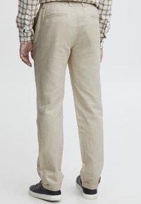 Lys beige bukser med en løs pasform, der har en elastisk talje og to baglommer. Kombineret med sorte sneakers.