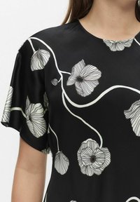 Czarna bluzka z krótkim rękawem w biało-szary wzór kwiatowy, z abstrakcyjnymi, szczegółowymi kwiatami i zakrzywionymi łodygami.