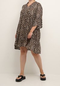 Vestido de estampado de leopardo con escote en V, mangas tres cuartos y dobladillo en capas. La tela ligera crea una silueta fluida.