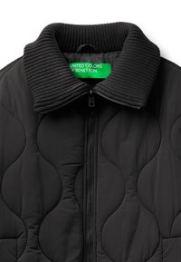 Černá prošívaná bunda s žebrovaným černým límcem a zapínáním na zip. Štítek zní "UNITED COLORS OF BENETTON." Hladká textura a jemný vzor.