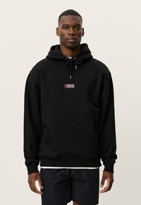 Μαύρη φούτερ με κουκούλα, τσέπη καγκουρό και ρυθμιζόμενο κορδόνι. Διαθέτει ένα μικρό πολύχρωμο λογότυπο στο στήθος. Μαλακή υφή υφάσματος.