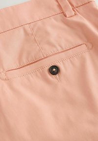 Poche arrière d'un pantalon rose clair avec fermeture à bouton et détail de couture visible.