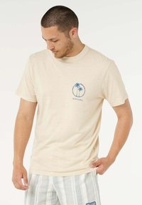 Maglietta beige in cotone con logo di una palma blu e grafica circolare. La maglietta ha una vestibilità classica con maniche corte.