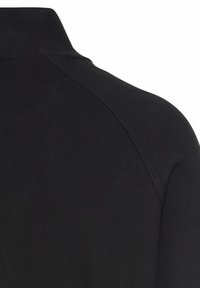Zwarte poloshirt van een textuurstof, met een klassieke kraag en schoudernaden. Het materiaal lijkt ademend en duurzaam.
