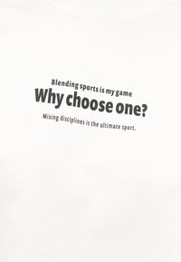 Κείμενο σε λευκό ύφασμα αναγράφει: «Το άθλημα μου είναι να συνδυάζω αθλήματα. Γιατί να επιλέξω μόνο ένα; Η ανάμειξη των πειθαρχιών είναι το απόλυτο άθλημα.»