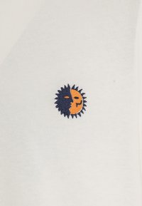 Camicia bianca con un design ricamato di sole e luna in blu navy e arancione. La texture è liscia con una forma aderente.