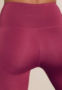 Hoch taillierte, pflaumenfarbene Leggings mit glatter Textur. Versehen mit einem dezenten Logo und verstärkten Nähten für erhöhte Haltbarkeit.