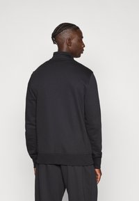 Μαύρο φούτερ με ψηλό γιακά, μακριά μανίκια και άνετη εφαρμογή. Διαθέτει ριμπ τελείωμα και μανσέτες, κατασκευασμένο από λείο ύφασμα.