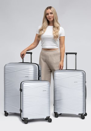 Trois valises rigides en argent de tailles variées, avec un motif en vagues texturé, des poignées rétractables et des roues roulettes lisses.