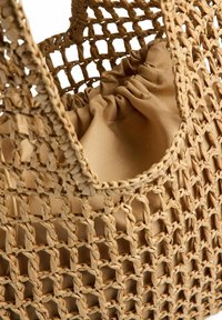 Sac en filet beige tissé avec une pochette en tissu froncée à l'intérieur, mettant en valeur la texture et le savoir-faire.