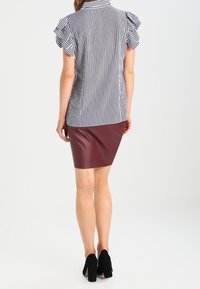 Randig blus med volangärmar i svart och vitt, parat med en figurnära bordeauxfärgad kjol. Svarta högklackade skor fulländar looken.