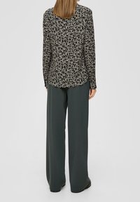 Blusa nera a maniche lunghe con stampa floreale e scollatura arrotondata, abbinata a pantaloni a gamba larga verde scuro, caratterizzati da una texture liscia e una vestibilità comoda.