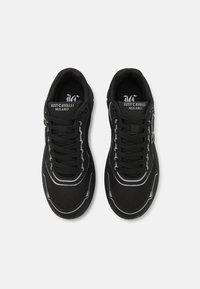 Zapatillas deportivas negras con upper de malla, diseño con cordones y acentos blancos contrastantes a lo largo de la suela y la marca.